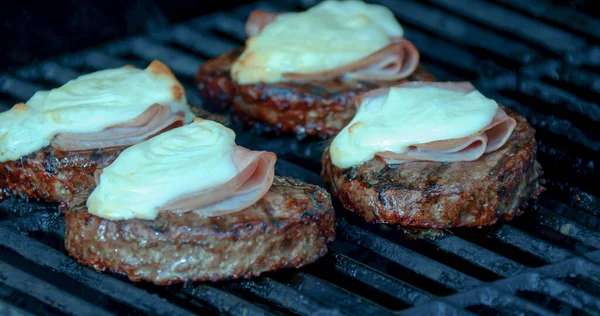 Cooking a burger patty with melted cheese and ham on a grill