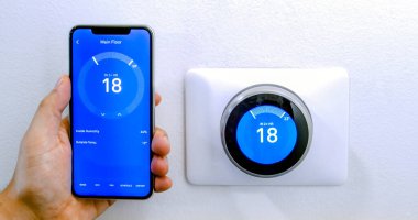 Calgary, Alberta, Kanada. 29 Ağustos 2020. Beyaz bir duvarda kablosuz Yuva Öğrenme Termostatı kullanarak Celsius metrikleri üzerine yuva uygulaması kullanan iPhone 11 Pro Max ile klima ile serinleyen bir kişi..