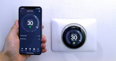 Calgary, Alberta, Kanada. 29 Ağustos 2020. iPhone 11 Pro Max ile enerji tasarrufu yapan bir kişi beyaz bir duvarda kablosuz Yuva Öğrenme Termostatı kullanarak Celsius metrikleri üzerine yuva uygulamasını kullanıyor..