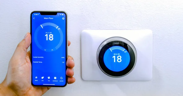 Calgary, Alberta, Kanada. 29 Ağustos 2020. Beyaz bir duvarda kablosuz Yuva Öğrenme Termostatı kullanarak Celsius metrikleri üzerine yuva uygulaması kullanan iPhone 11 Pro Max ile klima ile serinleyen bir kişi..