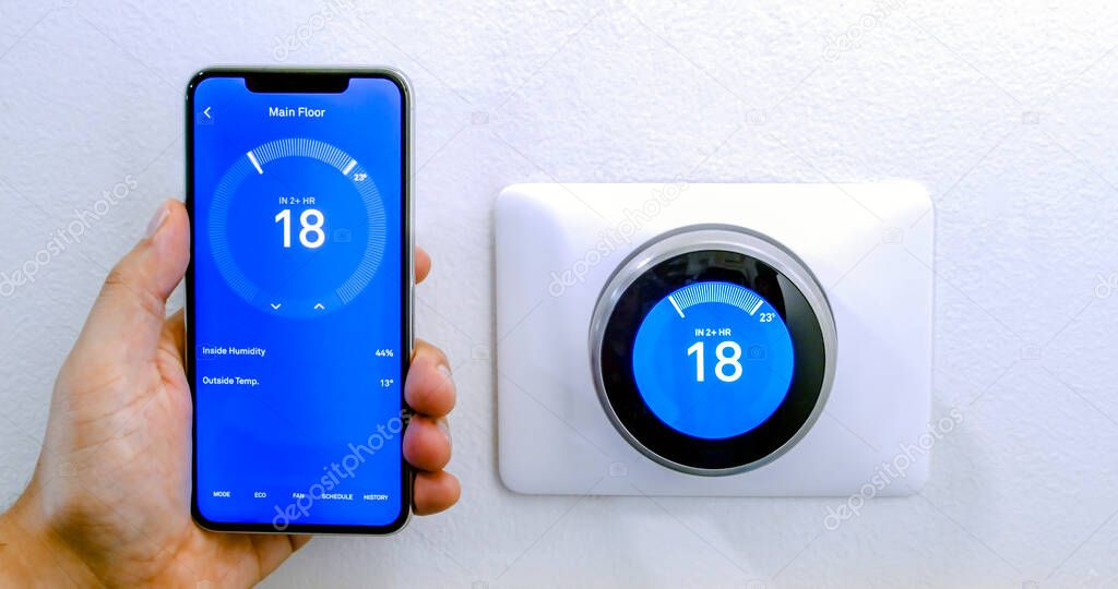 Calgary, Alberta, Canada. Aug. 29, 2020. A person cooling down with air conditioner with a iPhone 11 Pro Max using the nest app on celsius metrics using a wireless Nest Learning Thermostat on a white wall.