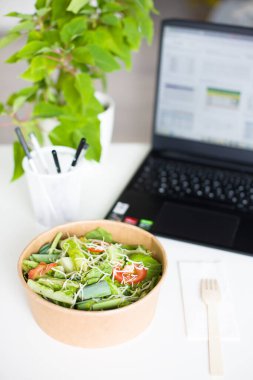 Çalışan bir masadaki bilgisayarın yanına yerleştirilmiş besleyici salata, iş ve sağlıklı yemek arasındaki denge kavramı. Yüksek kaliteli fotoğraf..