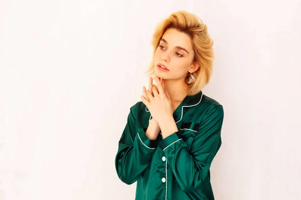 young blonde woman in green pajamas near withe wall looking left, copy space left
