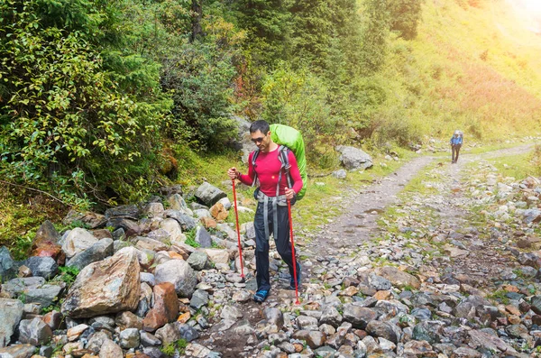 A handsome man with trekking poles walking along the pathway in the Tian Shan mountains