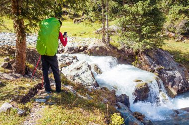 Bir dağ nehrinde küçük bir şelaleyi fotoğraflayan adam