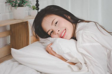 Çekici Asyalı genç ve güzel bir kadın. Yatakta ferahlatıcı bir şekilde uyanıyor..