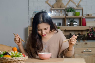 Mutfakta çorba içen mutlu genç bir kadın.