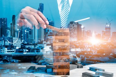 İş adamının çifte teşhirciliği ahşap blok ve şehir gece arkaplanı, iş kurma konsepti oluşturmaya çalışıyor