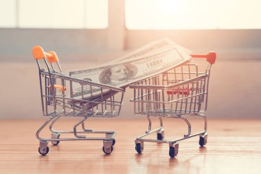 Para bankası, ahşap masada alışveriş arabasında bir dolar. Tüketiciler için parmak uçlarıyla kolay alışveriş. Çevrimiçi alışveriş ve teslimat hizmeti konsepti..