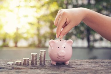 Kadın el ele tutuşan bozukluklar Piggy Bank 'a para yığını ile para koymak parktaki ahşap masaya basmak. Finansal konsept tasarrufu .retro klasik renk tonu.