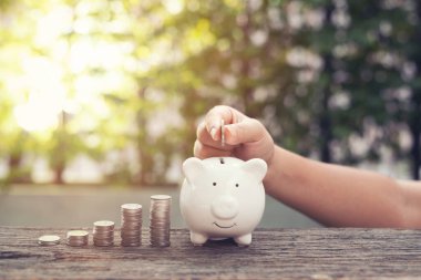 Kadın el ele tutuşan bozukluklar Piggy Bank 'a para yığını ile para koymak parktaki ahşap masaya basmak. Finansal konsept tasarrufu .retro klasik renk tonu.
