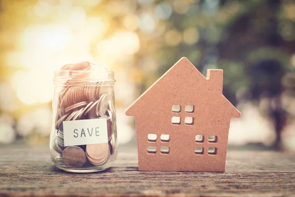 Model home with Coins in jar on wood table in the public park.money saving financial concept.retro vintage color tone.