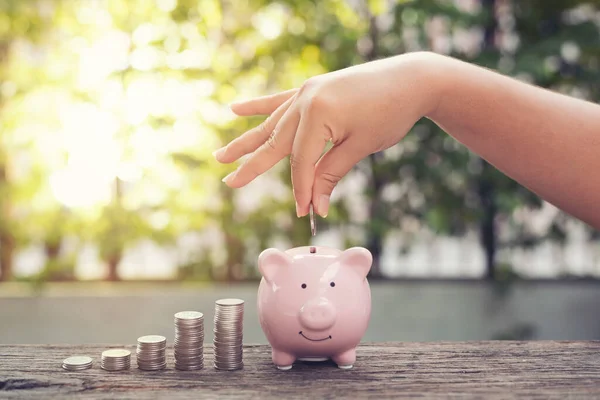Kadın el ele tutuşan bozukluklar Piggy Bank 'a para yığını ile para koymak parktaki ahşap masaya basmak. Finansal konsept tasarrufu .retro klasik renk tonu.