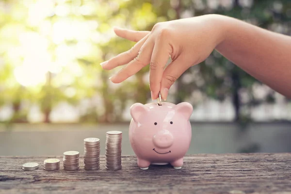 Kadın el ele tutuşan bozukluklar Piggy Bank 'a para yığını ile para koymak parktaki ahşap masaya basmak. Finansal konsept tasarrufu .retro klasik renk tonu.