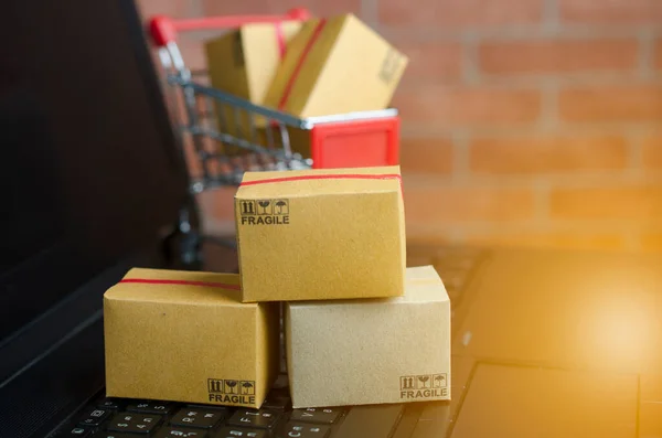 Dizüstü bilgisayarda, klavyede, tuğla zeminde bir sürü kutu var. Fikirler çevrimiçi alışveriş, tüketicilerin İnternet üzerinden doğrudan mal satın almalarına olanak sağlayan bir elektronik ticaret biçimidir..