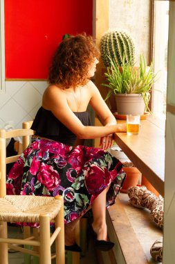 Bira ile ahşap bir taburede oturan bir pencereönünde bir barda bekleyen genç kadın