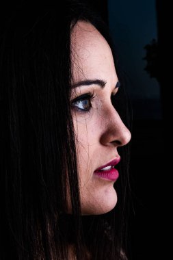 Stüdyo ışıklandırmalı portre, öne eğilmiş genç bir kadın, yüz profili.