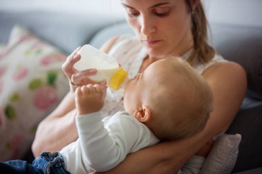 Anne, rahat evde kanepede oturuyor şişe, onun erkek bebek besleme