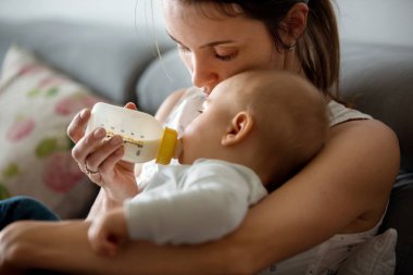 Anne, rahat evde kanepede oturuyor şişe, onun erkek bebek besleme