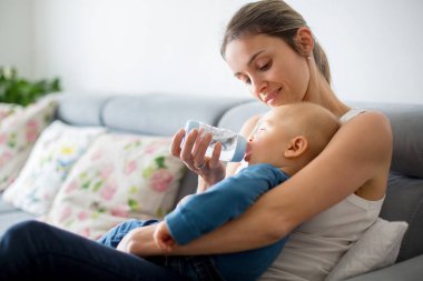 Anne, rahat evde kanepede oturuyor şişe, onun erkek bebek besleme