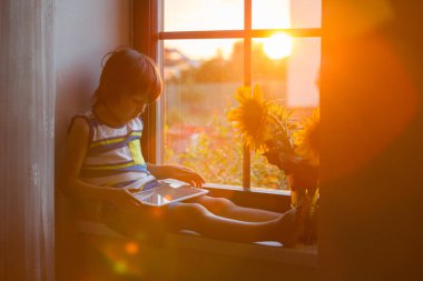 Bir pencerede tablet günbatımı üzerinde oynayan sevimli küçük yürümeye başlayan çocuk