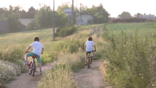 スポーティな子供 男の子兄弟 日没に一緒に農村風景にバイクに乗って — ストック動画