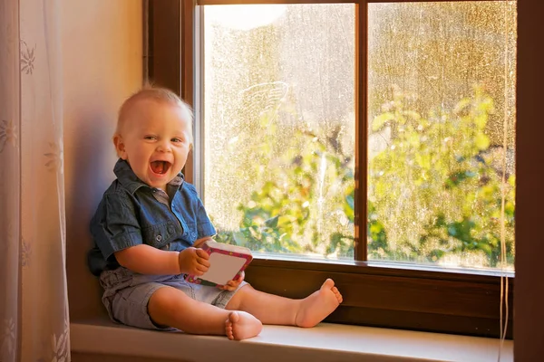 小男孩 可爱的孩子 坐在窗口在日落 愉快地玩婴孩书 — 图库照片