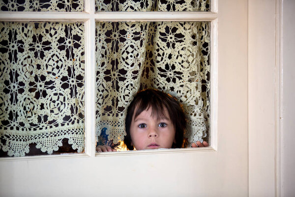 Маленький дошкольник, дитя, выглядывает испуганным через дверь с окнами
