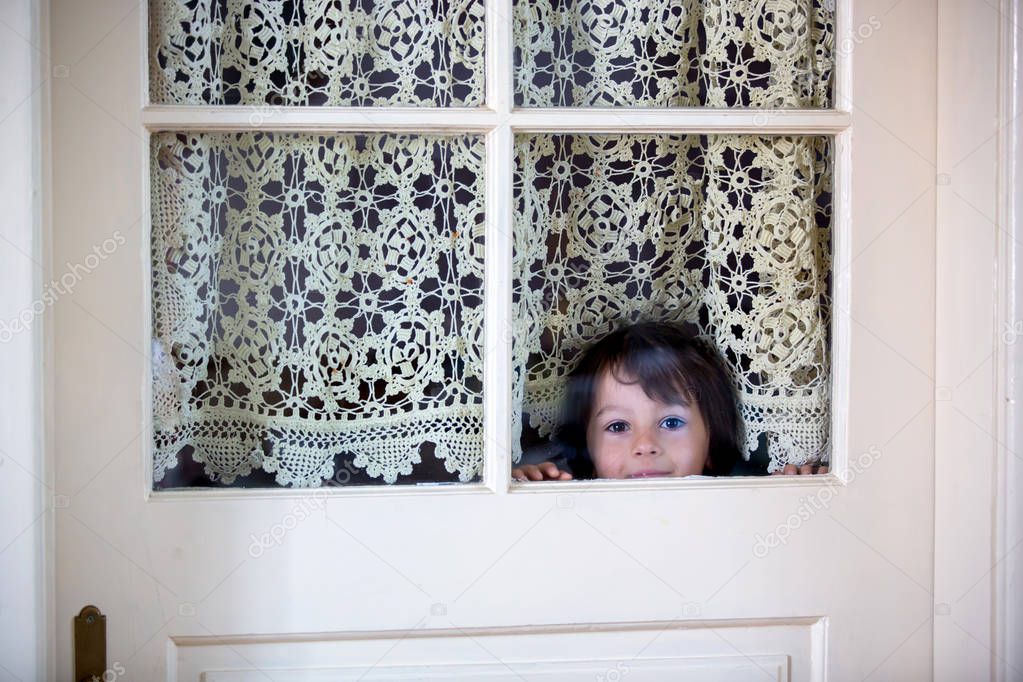 Little preschool boy, child, looking out scared through a door with windows