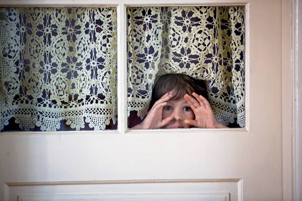 Маленький дошкольник, дитя, выглядывает испуганным через дверь с окнами
