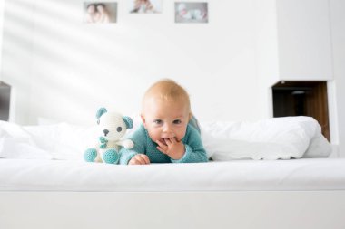 Mutlu bir şekilde beyaz güneşli, parlak yatak odasında kamera gülümseyen tutmak örme oyuncak, küçük şirin bebek çocuk, çocuk örme kazaklı,