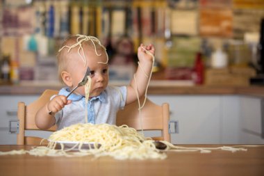 Küçük oğlu, yürümeye başlayan çocuk, spagetti yemek için yemek ve mutfak evde bir karışıklık yapmak