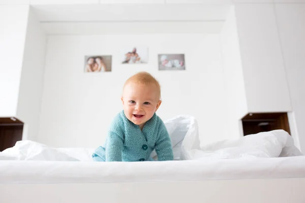 小さなかわいい赤ちゃん男の子 ニットのセーターの子白い日当たりの良い 明るい寝室でカメラで幸せそうに笑ってニット グッズを保持 — ストック写真