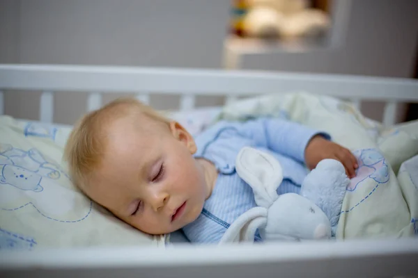 可爱的新生小男孩 晚上睡在婴儿床上 穿着白色睡衣的小男孩在暗室里打盹 Interi 灯和泰迪熊背景 — 图库照片