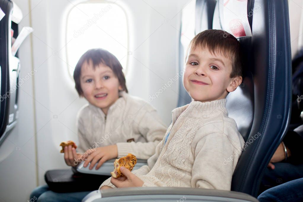 Two children, eating sandwiches on board in aricraft, traveling on vacation with paretns