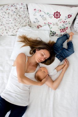 Yukarıdan sevgi ile yüksek açı çekim, sarılma, yatakta yatan anne ve yürümeye başlayan çocuk bebek çocuk. Mutlu aile concep