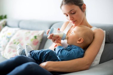 Anne, rahat evde kanepede oturuyor şişe, onun erkek bebek besleme