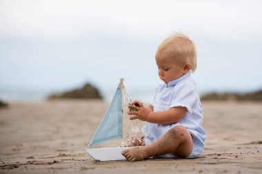 Sahilde su ve çalış bir oyuncak gemi ve oyuncak ayı ile yakın oturan erkek bebek
