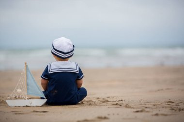 Sahilde su ve çalış bir oyuncak gemi ve oyuncak ayı ile yakın oturan erkek bebek