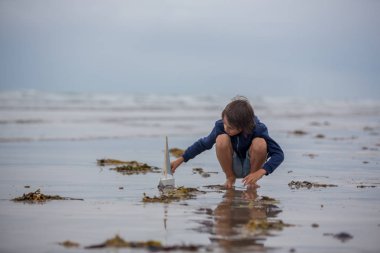 Çocuk kum ile kumsalda çalış. Oyuncak gemi plajındaki sevimli okul öncesi çocuk. Fırtınalı deniz sgore ve yaz tatile oynayan çocuk