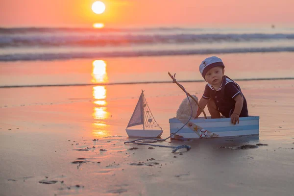 可爱的孩子 甜美的男孩 玩小船 泰迪熊和鱼在日落的海洋边缘 美丽的日落 — 图库照片