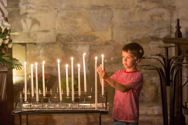 Little boy prays and puts a candle in Orthodox Church, sad kid with faith