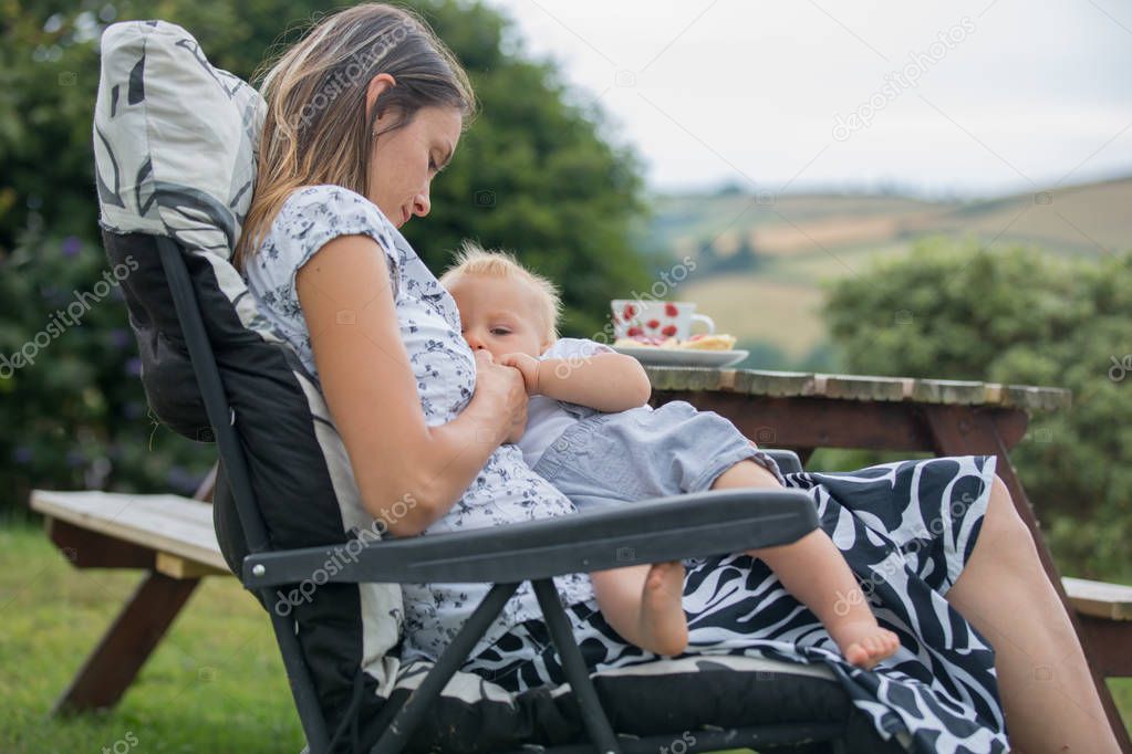 Young mother, holding her baby boy, breastfeeding him in the afternoon in her backyard, relax, zen, paece