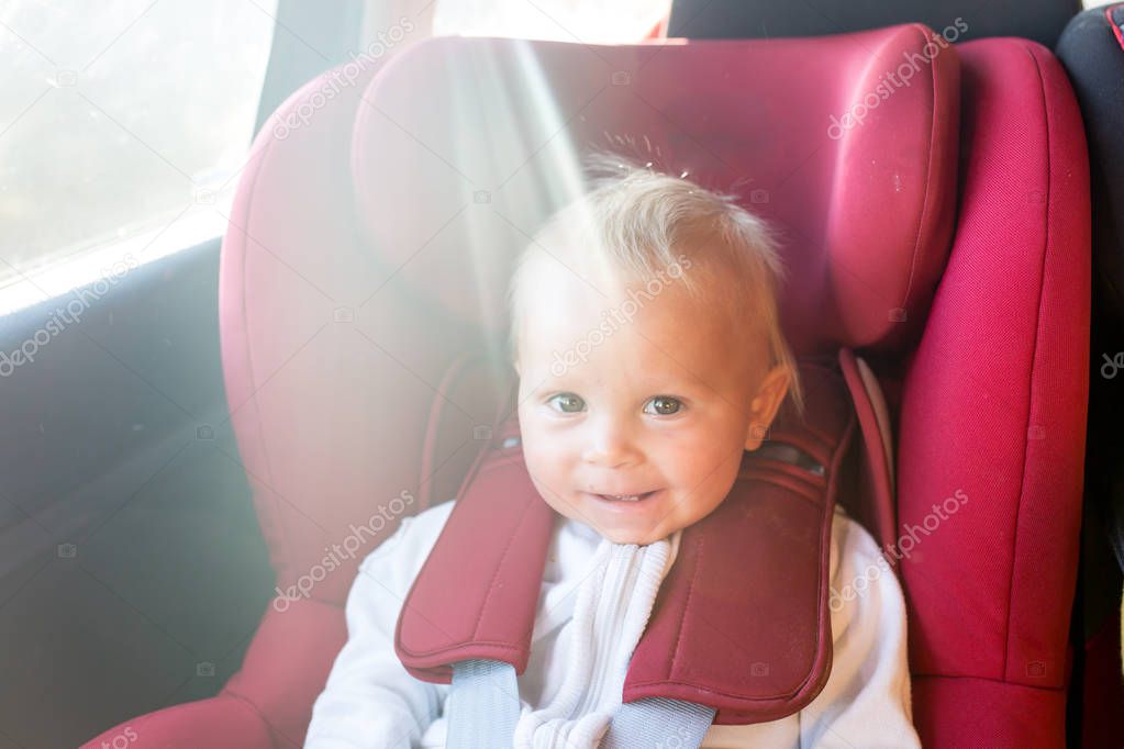 Portrait of cute white Caucasian toddler child, sitting in car seat looking in camera. Smiling baby in automobile vehicle fastened with seatbelt