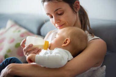 Anne, rahat evde kanepede oturuyor şişe, onun erkek bebek besleme