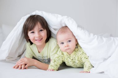 Sevimli küçük altı aylık bebeğim ve ağabeyi evde yatak yatak, yorgan altında oynarken, mutlu bir şekilde gülümseyerek 