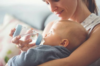 Anne, rahat evde kanepede oturuyor şişe, onun erkek bebek besleme