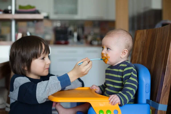 可爱的学龄前男孩 用捣碎的蔬菜喂他的小弟弟 宝宝第一次吃捣碎的食物 — 图库照片