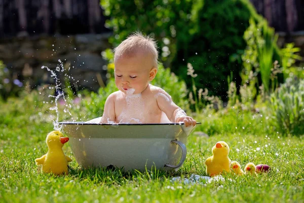 可爱的小蹒跚学步的男孩在盆里 在花园里沐浴着气泡和鸭子玩具 愉快地微笑着 — 图库照片
