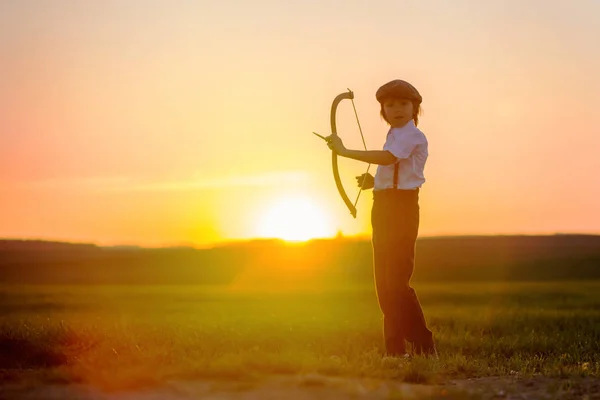 弓と矢 アーチェリーと遊ぶ子供のシルエットが夕日にターゲットで弓を撮影します — ストック写真